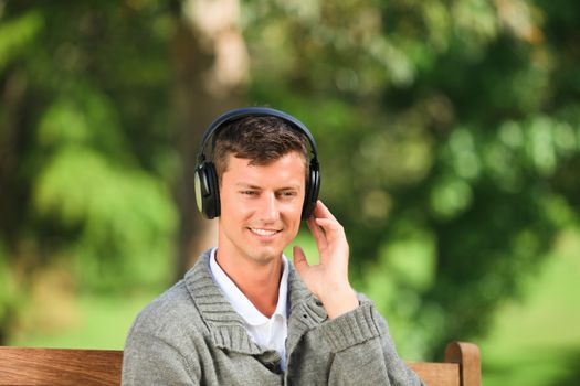 Young man listening to some music on the bench during the summer