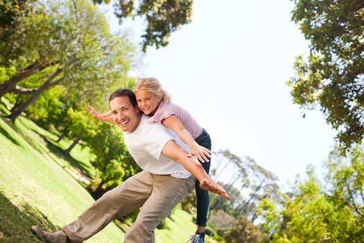 Little girl playing with her father in the park during the summer 