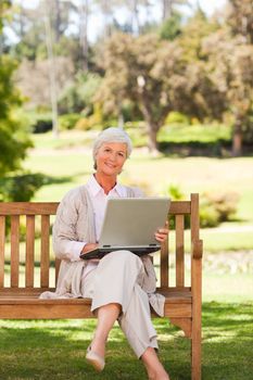 Retired woman working on her laptop in a park during the summer 