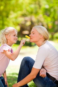 Mother and her daughter smelling a flower in a park during the summer 
