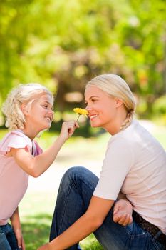 Mother and her daughter smelling a flower during the summer in a park