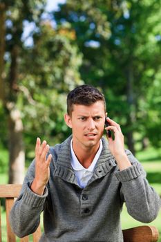 Young man phoning on the bench during the summer 