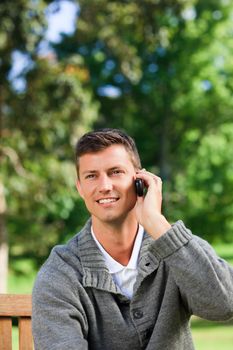 Young man phoning on the bench during the summer 