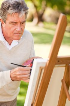 Elderly man painting in the park during the summer