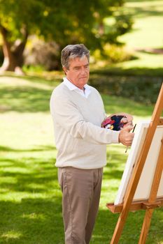 Elderly man painting in the park during the summer