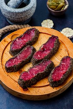 Stone mortar bowl with pestle, garlic, bay leaf and wooden cutting board with raw pepper steaks on stone surface