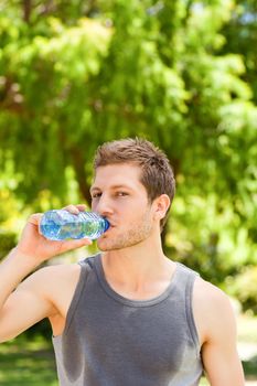 Sporty man drinking water in the park during the summer
