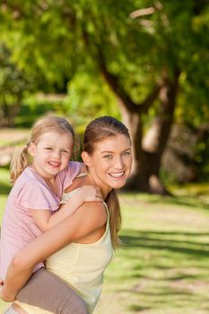 Beautiful mother giving daughter a piggyback during the summer