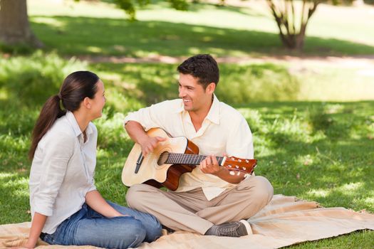 Romantic man playing guitar for his wife in a park