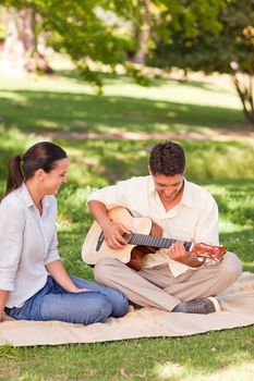 Romantic man playing guitar for his wife in a park