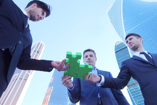 Business people assembling jigsaw puzzle near skyscrapers