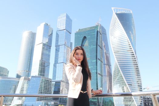 Young beautiful businesswoman with cellphone outdoors at skyscraper background