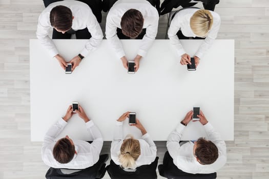 Business people using smartphones sitting at table in office, white copy space background