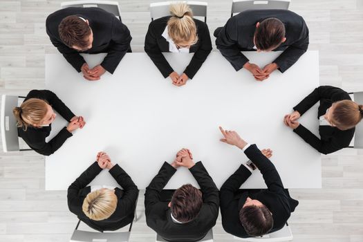 Business people sitting around empty table, business man pointing to blank copy space in the middle