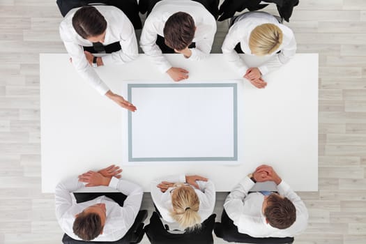 Business people sitting around empty table, business man pointing to blank copy space in the middle