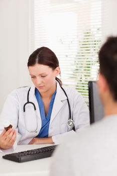 A female doctor is looking at a can of pills next to a patient