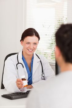 A female doctor is showing pills to a patient in her office