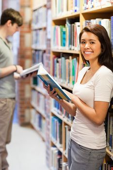 Portrait of a smiling student while holding a book in a library