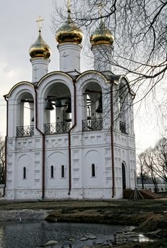 White orthodox church with a golden dome on a background of tree branches in early spring