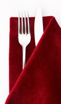 Knife and fork wrapped in red napkin as a table setting  on a white background 