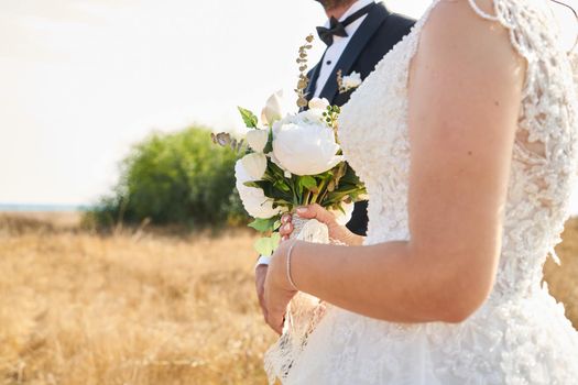 Wedding flowers bouquet in bride's hand. Bridegroom stands on the field with bride in wedding dress. This image was taken on OCT 2016, on outside a church Goa, India.