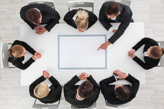 Business people sitting around empty table, business man pointing to blank copy space in the middle