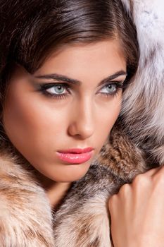 Young beautiful woman in a fur coat on a studio background