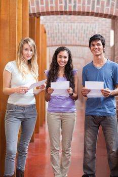 Portrait of smiling students holding a piece of paper in a corridor
