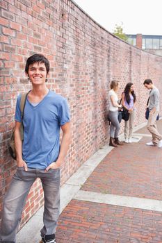 Portrait of a student posing while his friends are talking outside a building