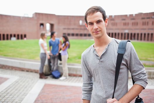 Serious student posing while his classmates are talking in a yard