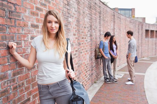 Cute student posing while her friends are talking outside a building