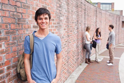 Male student posing while his friends are talking outside a building