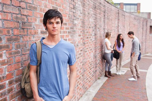 Student posing while his friends are talking outside a building
