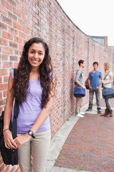 Portrait of a smiling student posing while her friends are talking outside a building