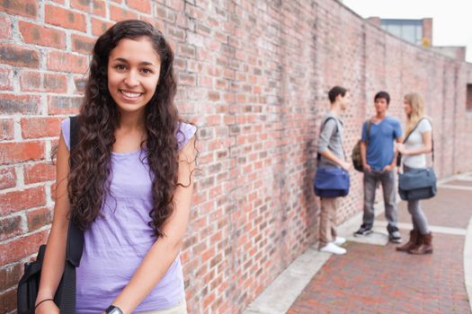 Smiling student posing while her friends are talking outside building
