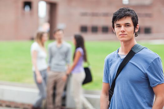 Handsome student posing while his classmates are talking in a yard
