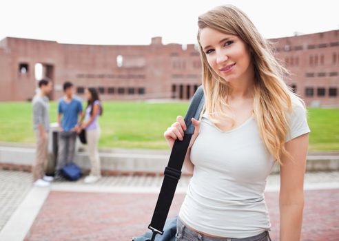 Blondhaired student posing while her friends are talking in a yard