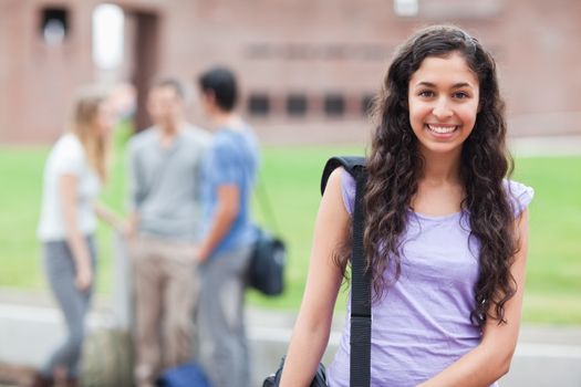 Cute student posing while his classmates are talking in a yard