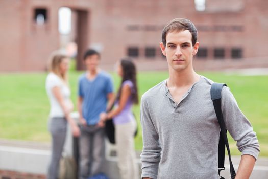 Male student posing while his classmates are talking in a yard