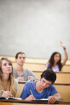 Portrait of students taking notes while their classmate is raising her hand in an amphitheater