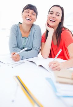 A laughing pair of girls at the table as they do some homework 