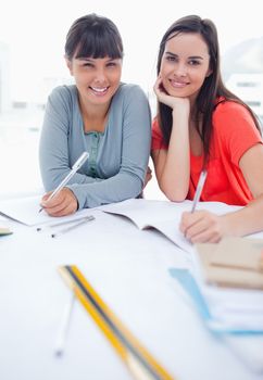 A couple of girls smiling as they look at the camera while doing some homework