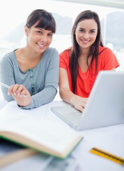 A close up shot of two smiling girls sitting in front of a laptop and some books