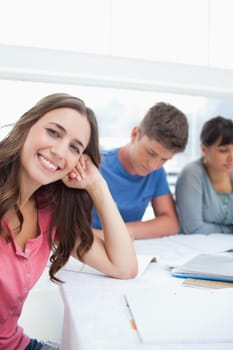 A smiling woman beside her friends looking into the camera with her head resting on her hand