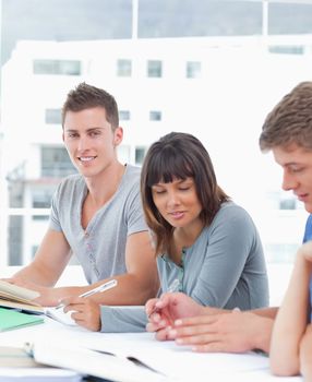 A smiling man looks into the camera while his friends look at their books and study