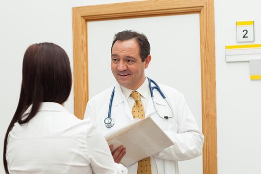 Smiling doctor holding a file while talking to a woman in a hallway