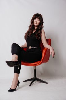 Young beautiful girl in business suit, shoes sitting on red chair, white background, business lady, young cute brunette