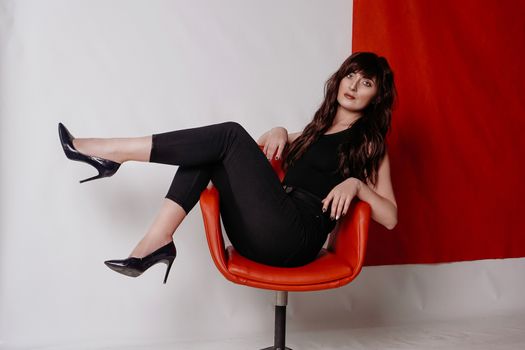 Young beautiful girl in business suit, shoes sitting on red chair, white background, business lady, young cute brunette