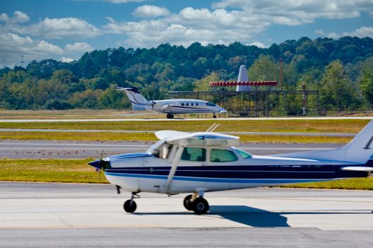 A propeller plane taxiing for takeoff while a jet is landing in the distance. Focus on Jet