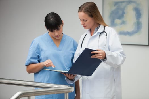 Female doctor explaining notes to nurse and pointing in hospital corridor